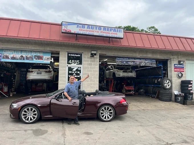 A burgundy convertible sports car parked in front of JJ Auto Repair shop with a person standing beside it